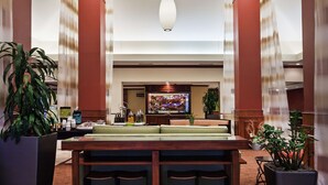 A lobby with a reception desk, large hanging pendant lights, and potted plants. - Hilton Garden Inn Corpus Christi (Corpus Christi)