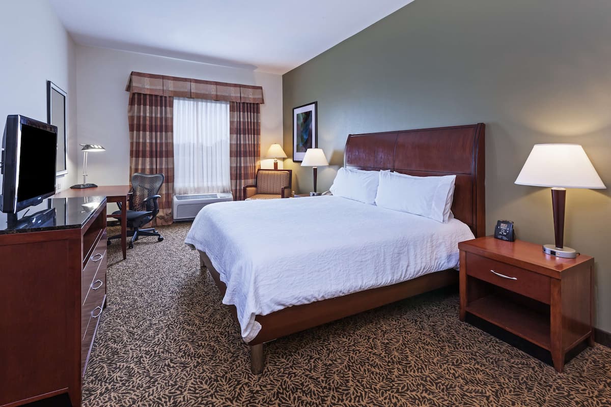 A hotel room with a large bed, a desk with a computer, a chair, and two bedside tables with lamps.