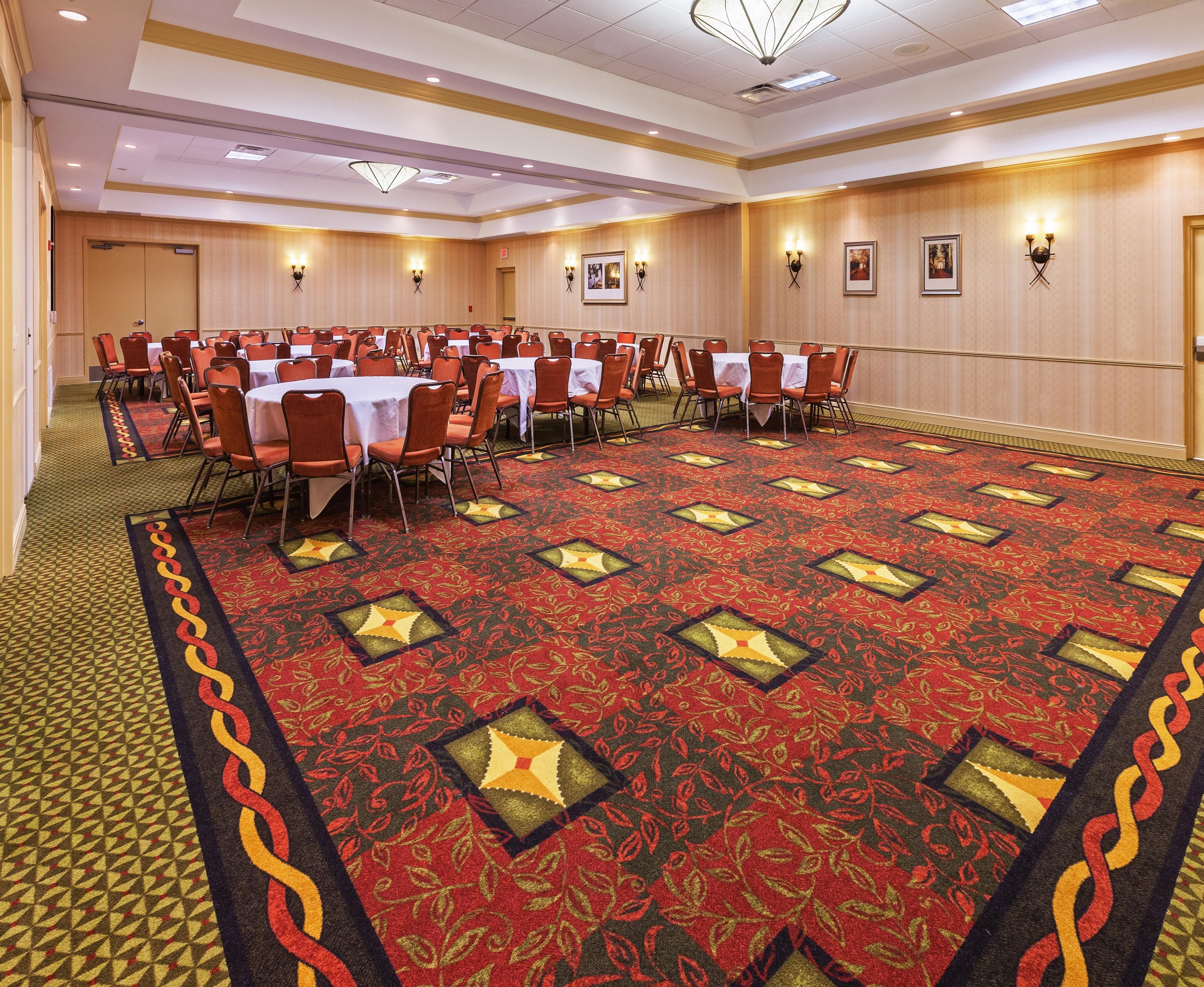 Un salón de conferencias con mesas y sillas, piso alfombrado e iluminación en la pared.
