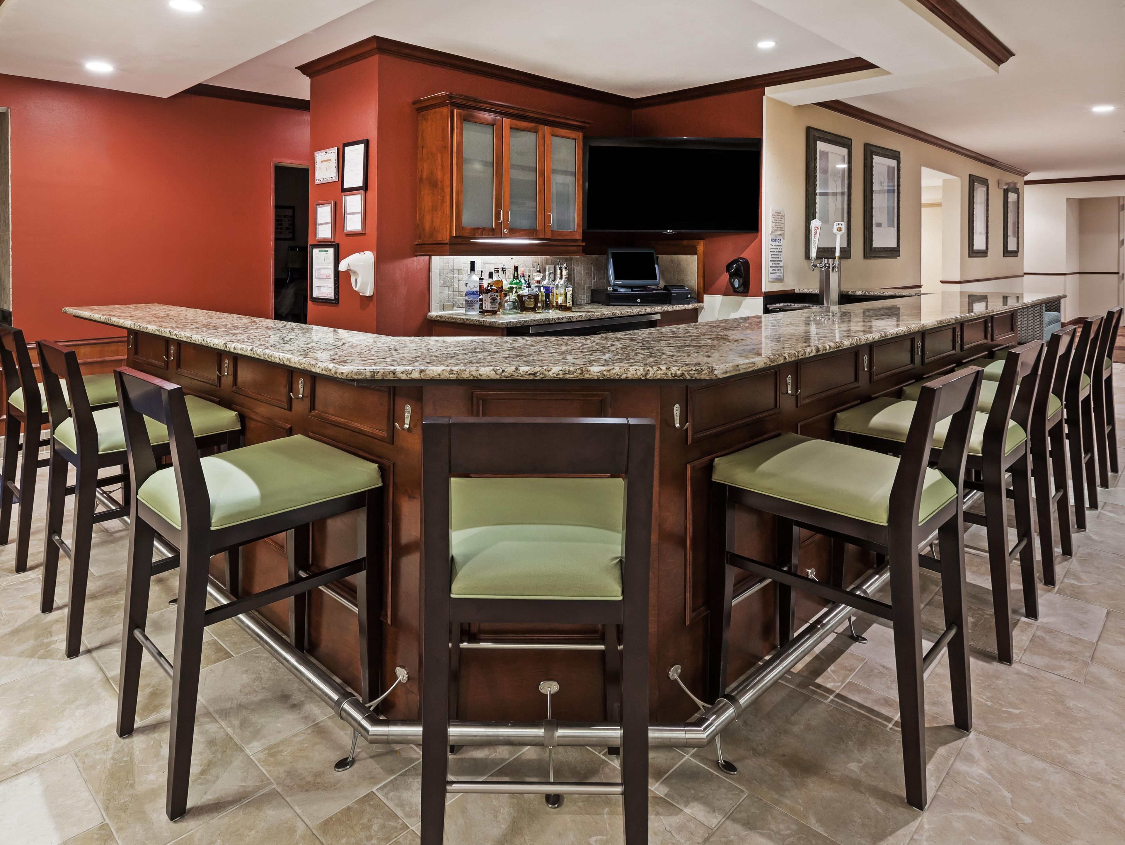 A bar area with a granite countertop, multiple bar stools, and a kitchen area with wooden cabinets and a built-in TV.