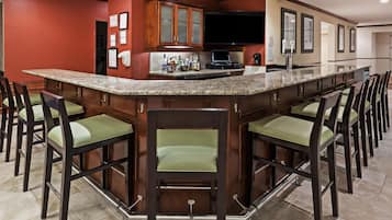 A bar area with a granite countertop, multiple bar stools, and a kitchen area with wooden cabinets and a built-in TV.