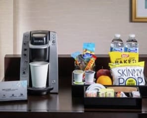 Una kitchenette con una cafetera, una taza, una caja de Skinny Pop y varios aperitivos.