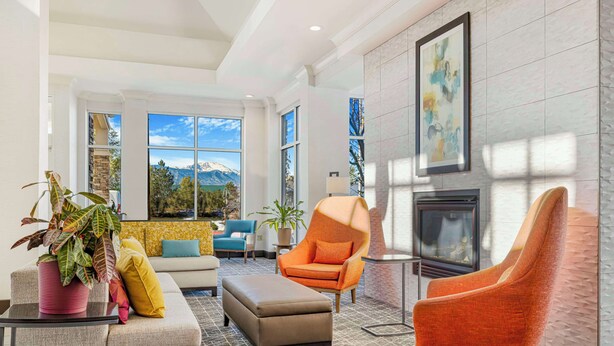 A modern living room with a sofa, ottoman, and two armchairs. There is a fireplace and a large window with a mountain view.