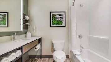 A modern bathroom with a white sink, toilet, and bathtub. There are framed pictures on the wall and a shelf with towels.