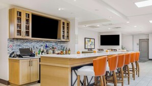 A modern kitchen with a bar area, wooden cabinets, and a large flat-screen TV.
