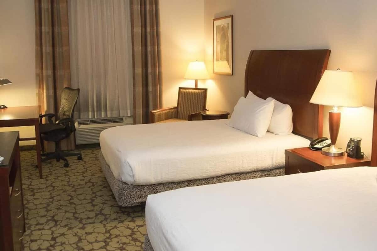 Habitación de hotel con dos camas, un escritorio, una silla, una lámpara y un teléfono en la mesita de noche.
