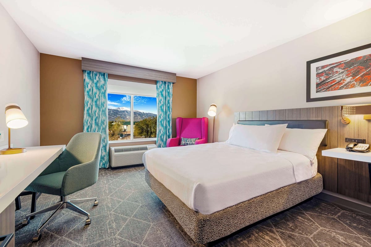 Habitación de hotel con cama, escritorio, silla, mesita de noche y ventana con cortinas.