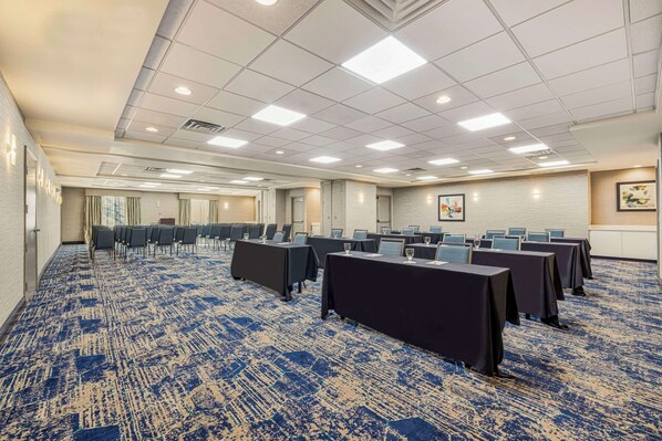 A conference room with rows of tables, chairs, and a carpeted floor.