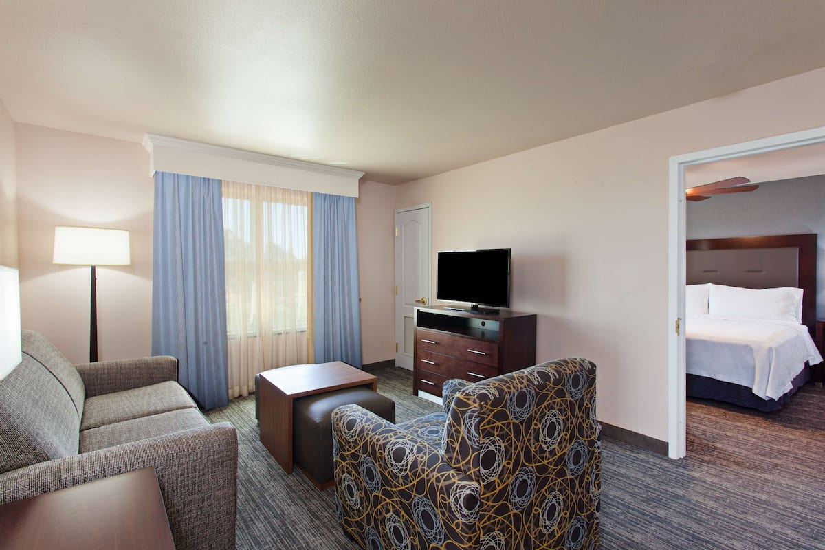 Una habitación de hotel con sofá, sillón, televisión, escritorio y cama.