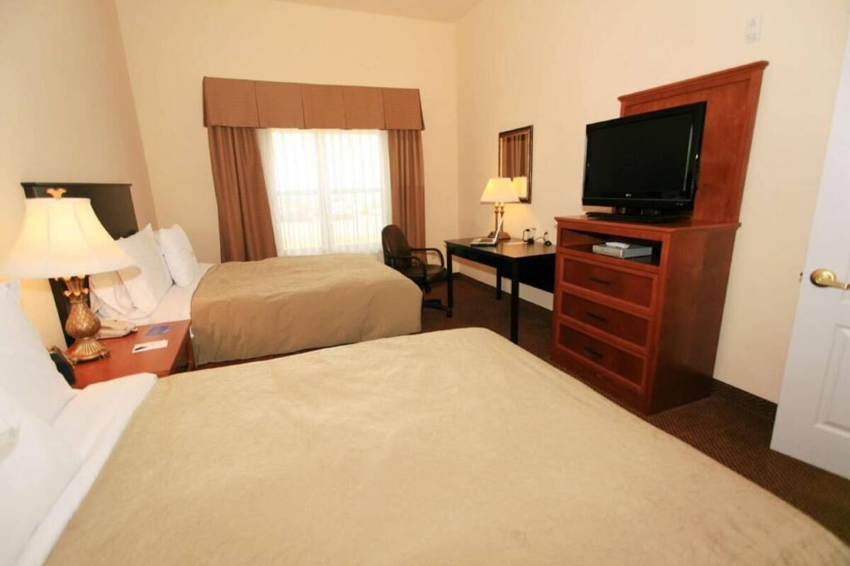 Habitación de hotel con dos camas, un escritorio, un televisor y una ventana con cortinas.