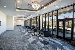 A spacious hallway with a checkered carpet, rows of seating, large windows, and a chandelier. - Hilton Dallas/Southlake Town Square (Southlake)