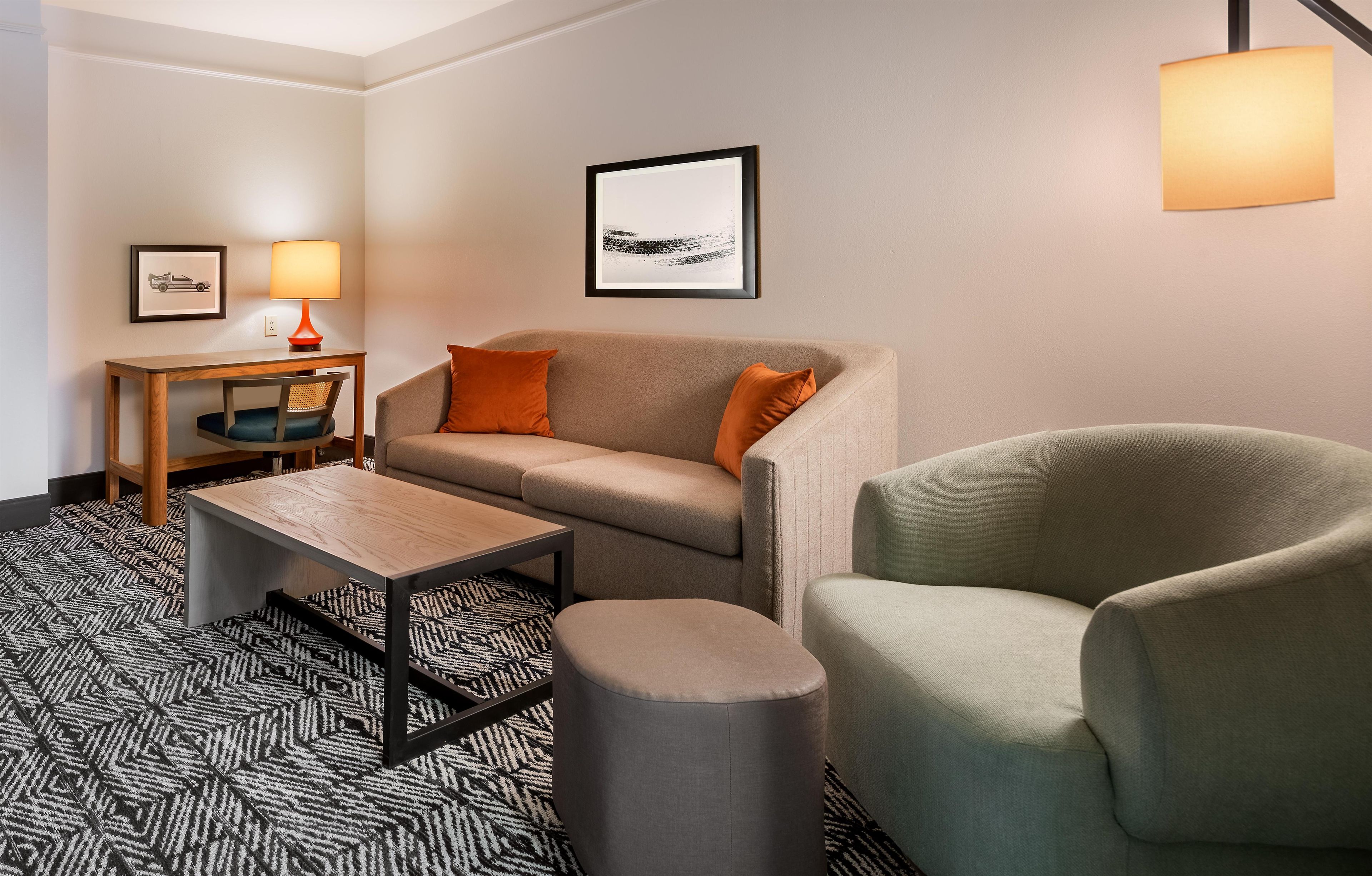 Habitación de hotel con sofá, sillón, mesita, lámpara y un cuadro en la pared.