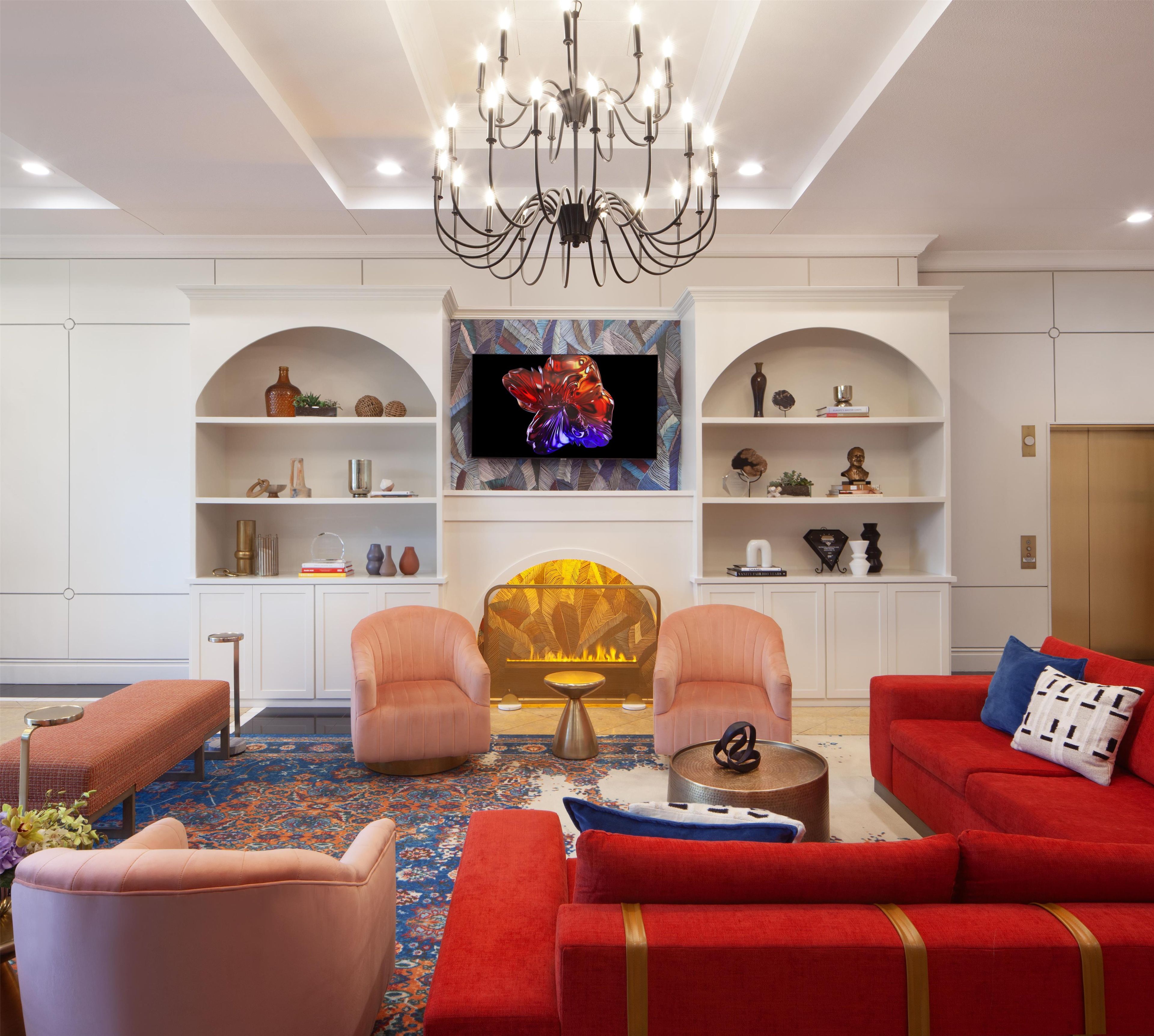 A modern living room with a fireplace, two armchairs, a red sofa, and a chandelier.