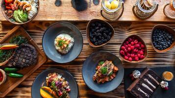 A variety of dishes on a wooden table, including grilled steak, salmon, and various fruits and vegetables.