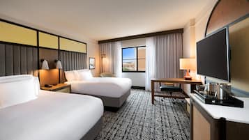 A hotel room with two beds, a desk with a television, and a window with a view.