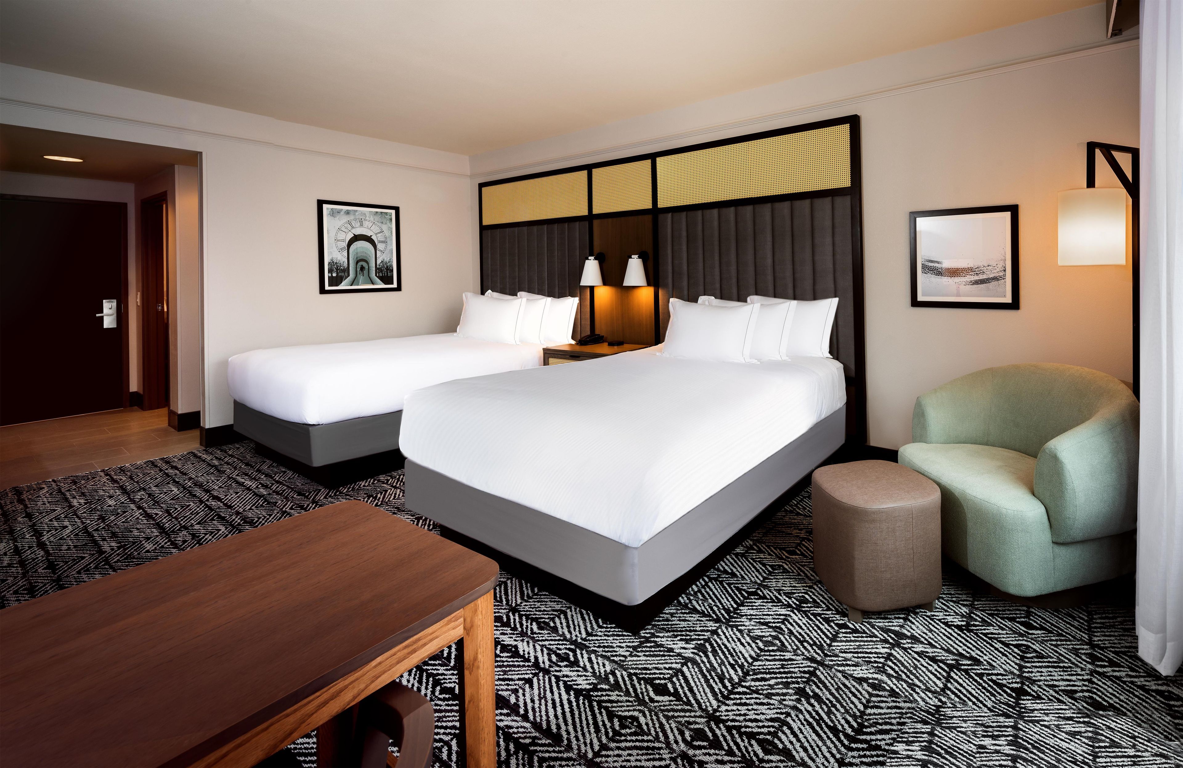 A hotel room with two beds, a desk, a chair, and a patterned carpet.