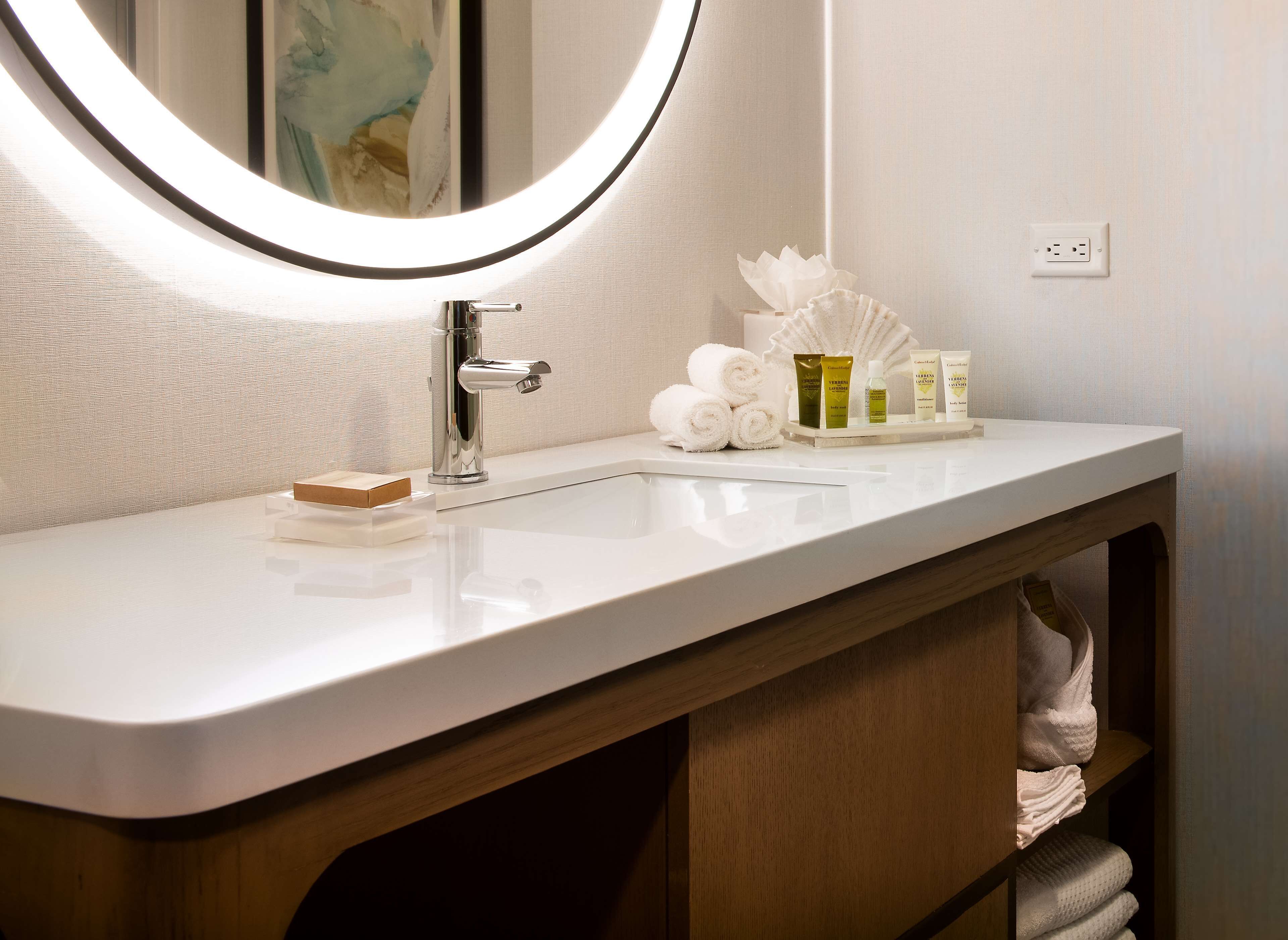 Une salle de bain avec un lavabo blanc, un miroir avec un éclairage intégré et des articles de toilette posés sur le comptoir.