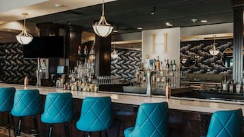 A bar area with multiple stools, a well-stocked bar counter, and a large H sign on the wall.