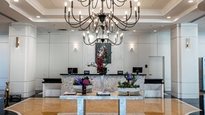 A spacious lobby with a large chandelier, marble flooring, and a reception desk with a vase of flowers. - Hilton Dallas/Southlake Town Square (Southlake)
