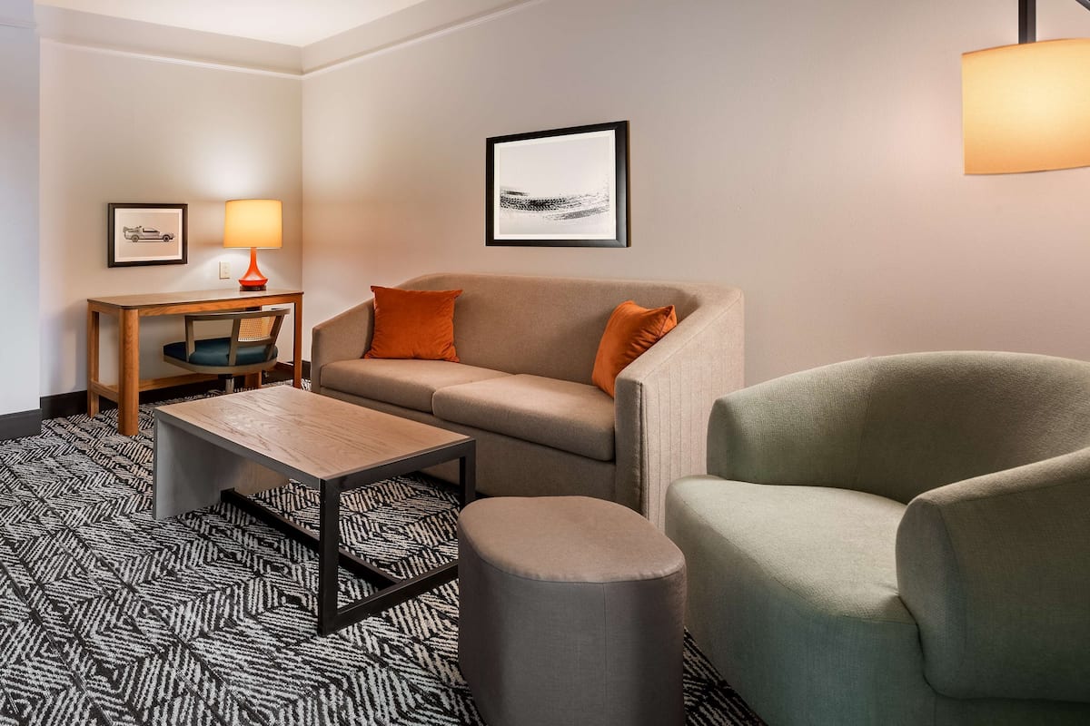 A modern hotel room with a sofa, armchair, small table, and a lamp.