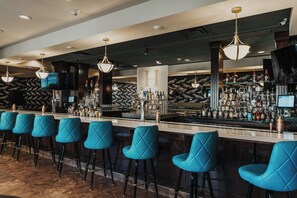A bar area with multiple stools, a bar counter, and a variety of bottles and glasses. - Hilton Dallas/Southlake Town Square (Southlake)