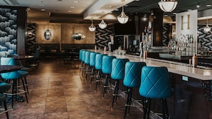 A bar area with a long counter, multiple bar stools, and a variety of bottles and glasses. - Hilton Dallas/Southlake Town Square (Southlake)