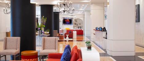 A modern hotel lobby with a red sofa, beige armchairs, a white coffee table, and a black column.