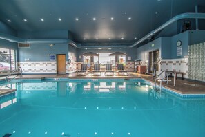 An indoor swimming pool with a view of the sky through the ceiling, a clock on the wall, and a notice board.