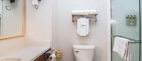 A bathroom with a toilet, a sink, a mirror, and a glass shower enclosure.