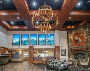 A lobby with a chandelier, mountain view paintings, a fireplace, and seating area.