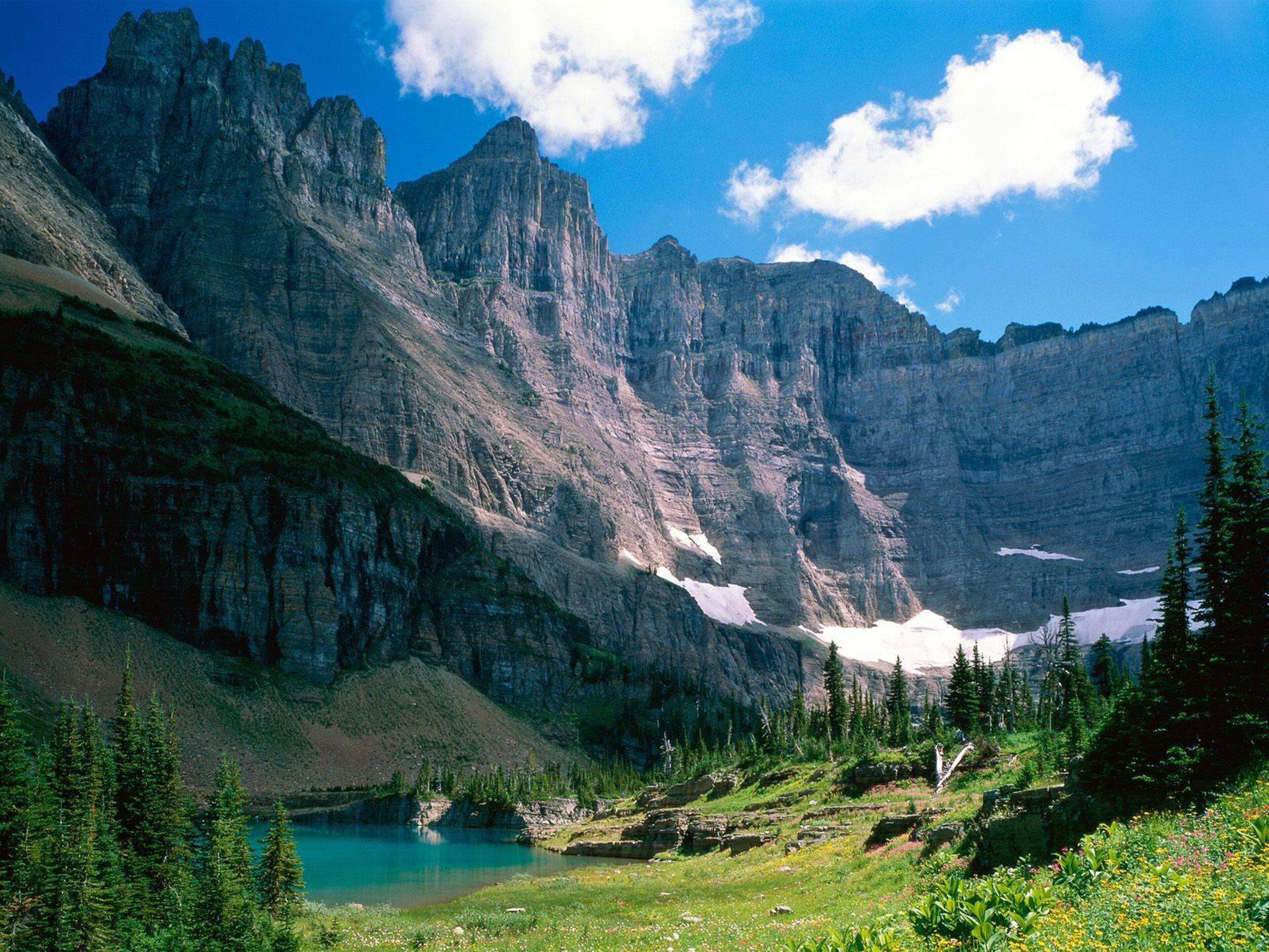 Un paysage montagneux avec un lac, une forêt dense et des falaises rocheuses.