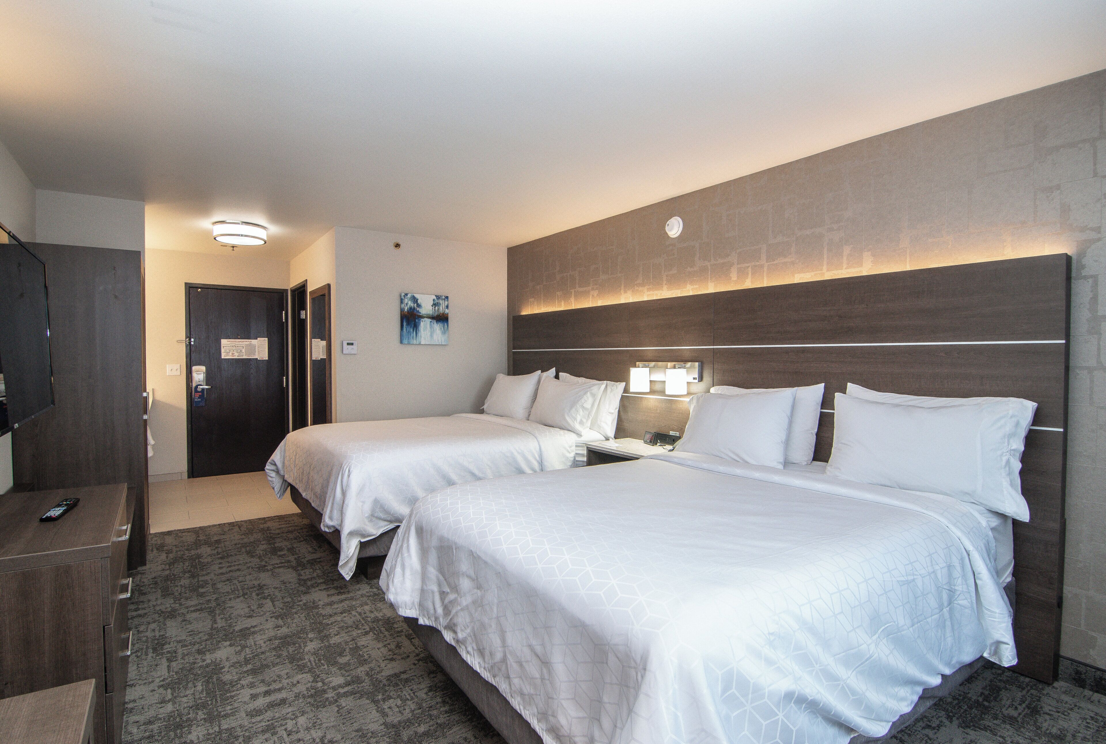 Habitación de hotel con dos camas, un escritorio y un mando a distancia, y una lámpara fijada a la pared.