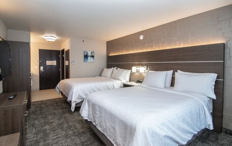 A hotel room with two beds, a desk with a chair, a dresser, and a nightstand with a lamp.