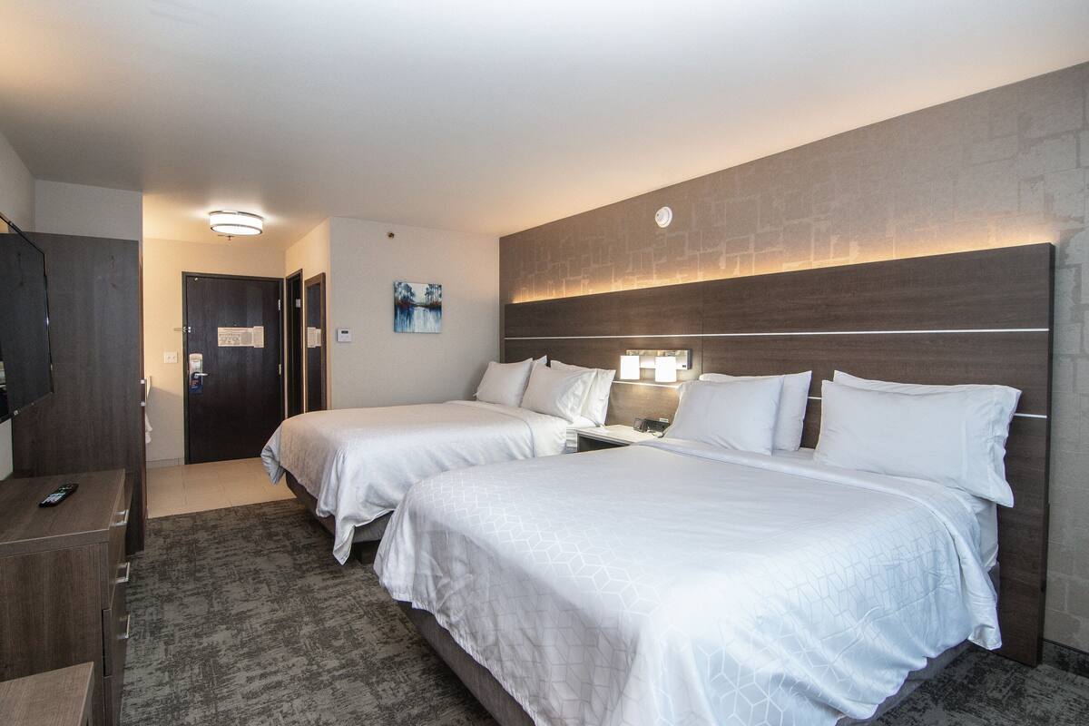Habitació d'hotel amb dos llits, un escriptori amb cadira, un armari i una tauleta de nit amb làmpada.