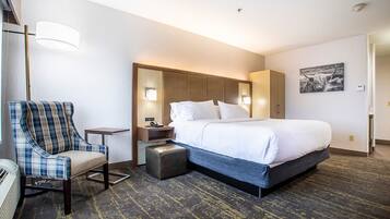Una habitación de hotel con una cama grande, una silla, una mesita de noche y una lámpara.