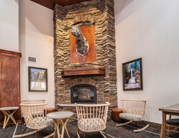 A stone fireplace with a deer head above it, surrounded by wooden chairs and a table.