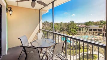 A balcony with a table and chairs, a ceiling fan, and a view of a swimming pool and buildings.