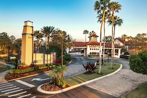 A gated entrance to The Berkley, Orlando, a vacation village resort with a prominent tower, palm trees, and a paved driveway.