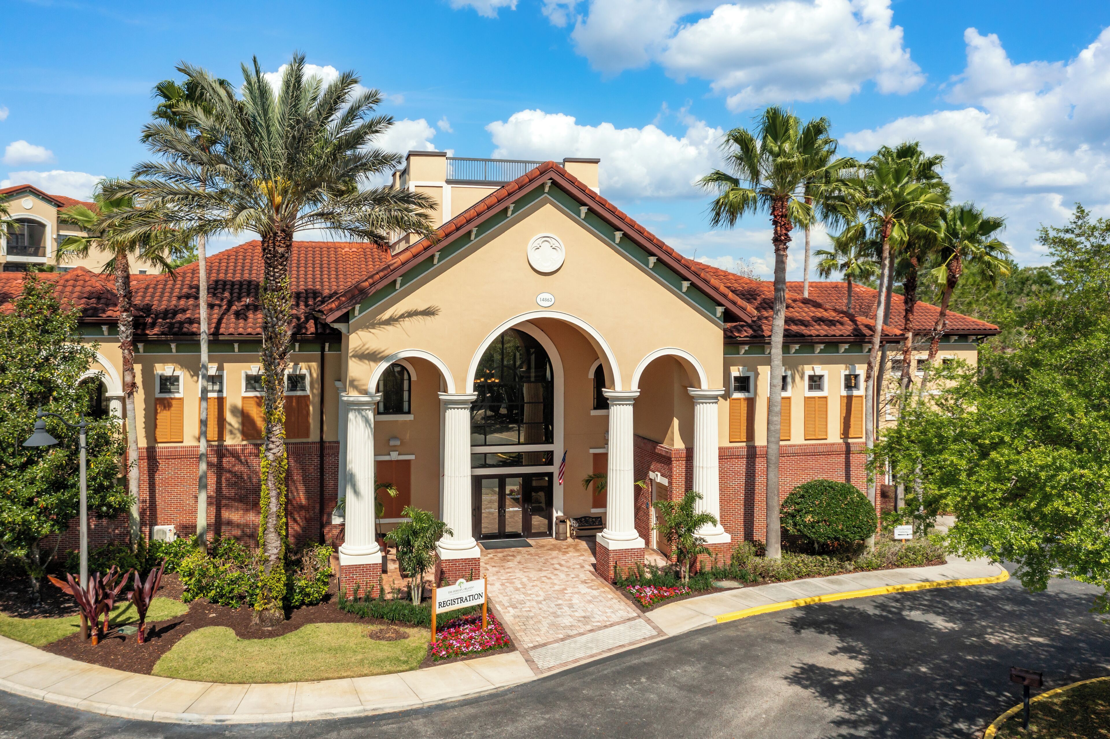 A building with a beige facade, red-tiled roof, and arched entrance.
