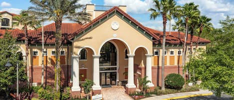 A building with a beige facade, red-tiled roof, and arched entrance.