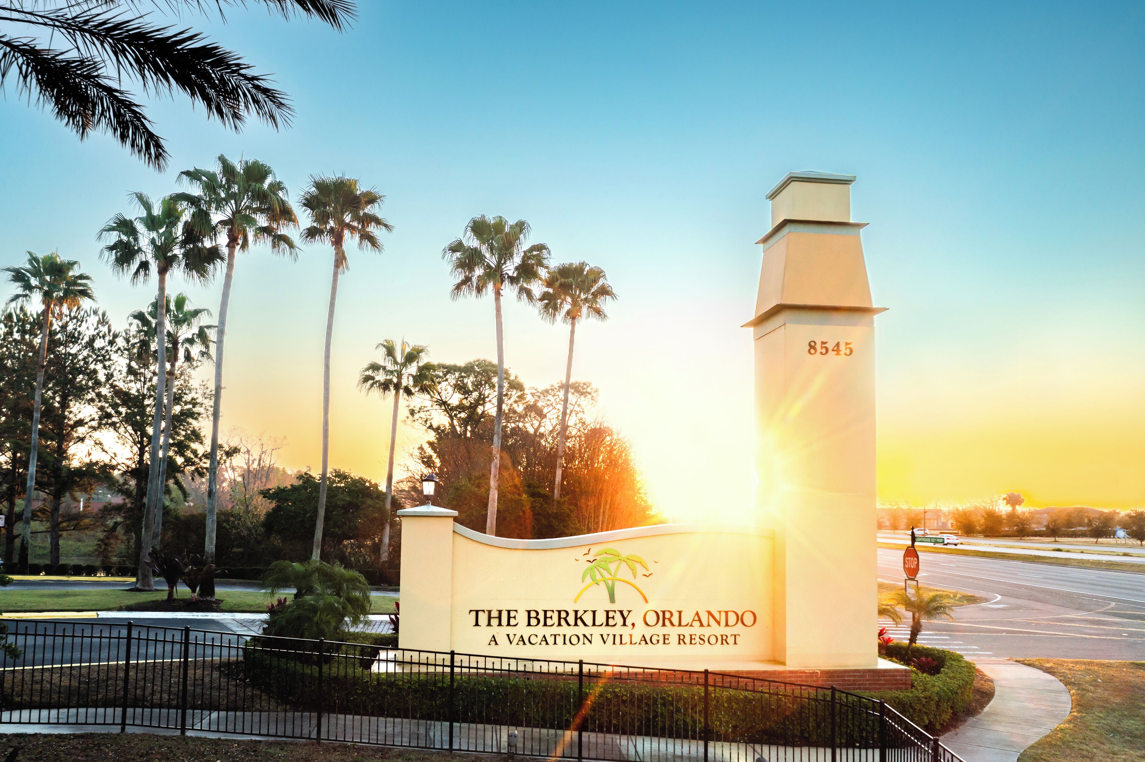 A sign for The Berkley, Orlando, a vacation village resort, with palm trees and a clear sky.