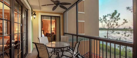 A balcony with a table and chairs, a ceiling fan, and a view of a body of water.