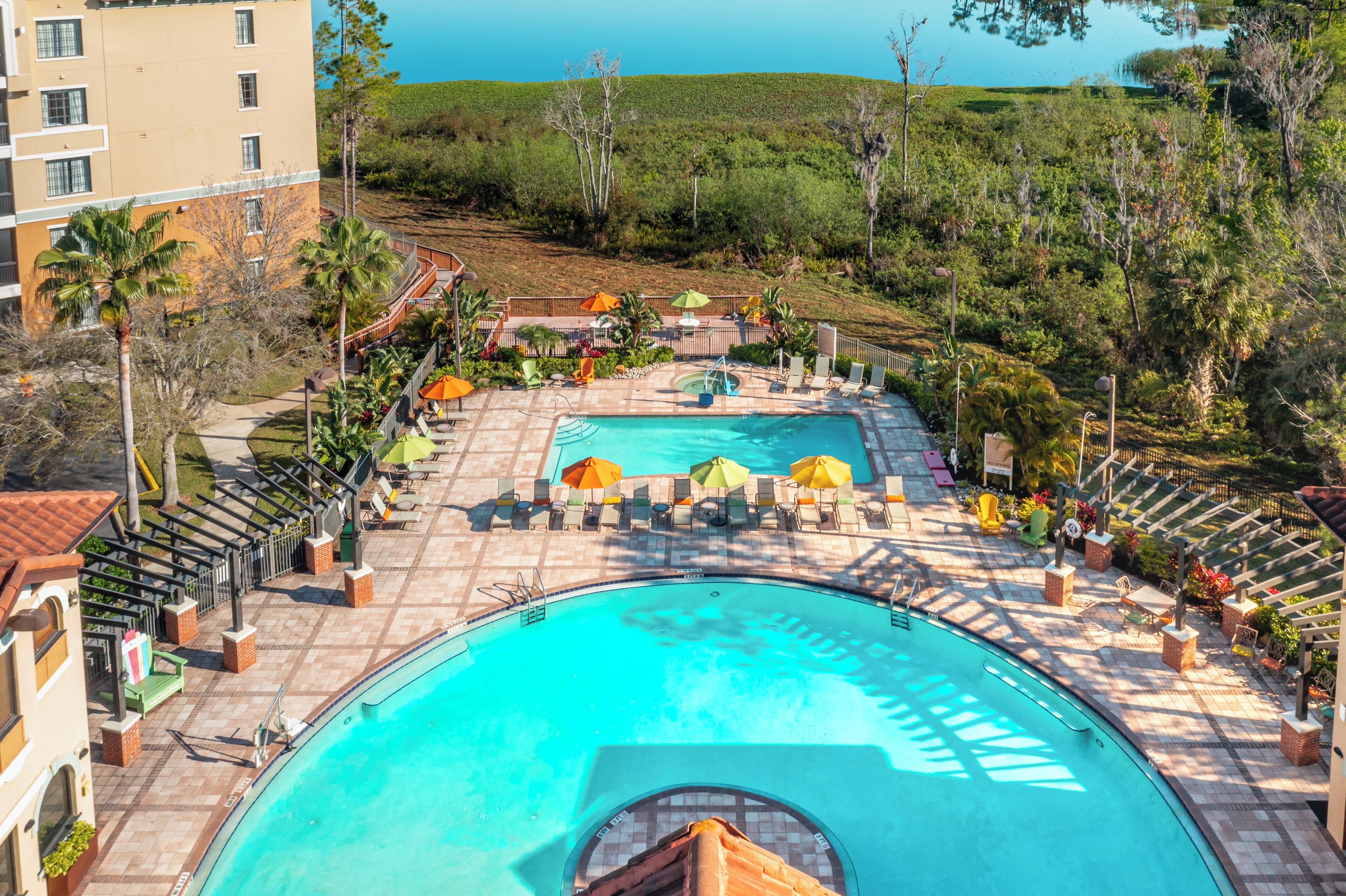A resort pool area with a large pool, lounge chairs, umbrellas, and a view of the ocean.
