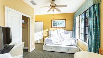 Una habitación de hotel con cama, escritorio con computadora, ventilador de techo y ventana con cortinas.