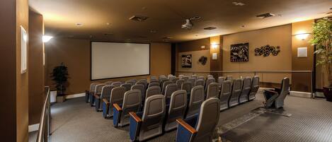 A conference room with rows of chairs, a projector screen, and a large potted plant.