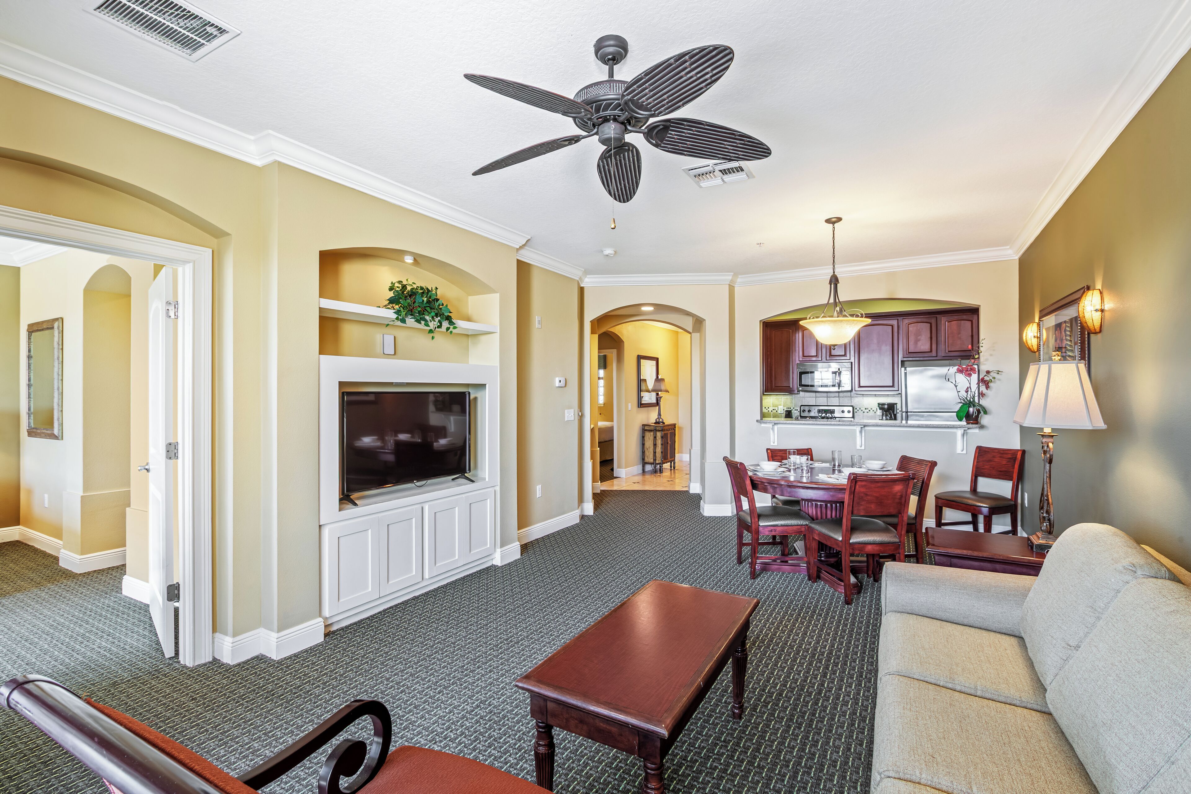 A spacious living room with a flat-screen TV, a ceiling fan, and a dining area with wooden chairs and a table.