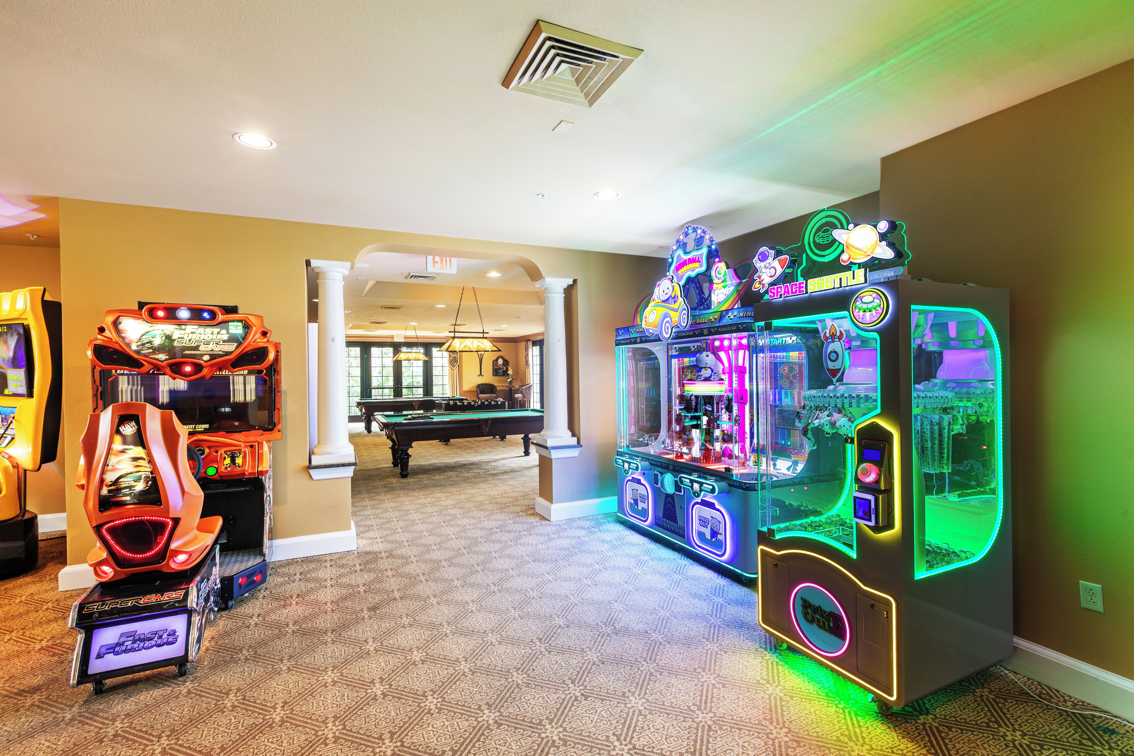 A hotel lobby with arcade games, a pool table, and a neon-lit claw machine.