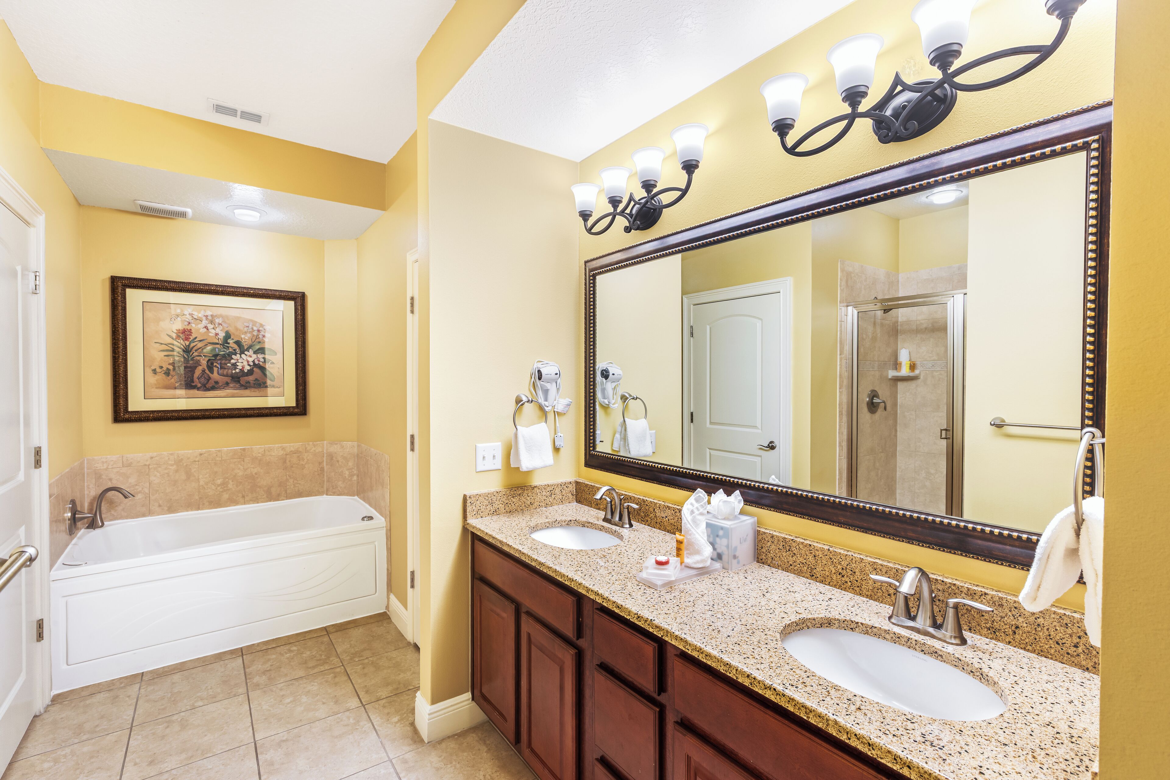 A bathroom with a bathtub, two sinks, a large mirror, and a framed picture on the wall.