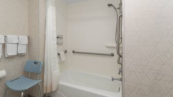 A bathroom with a bathtub, a shower, a handrail, a towel rack, and a blue chair.