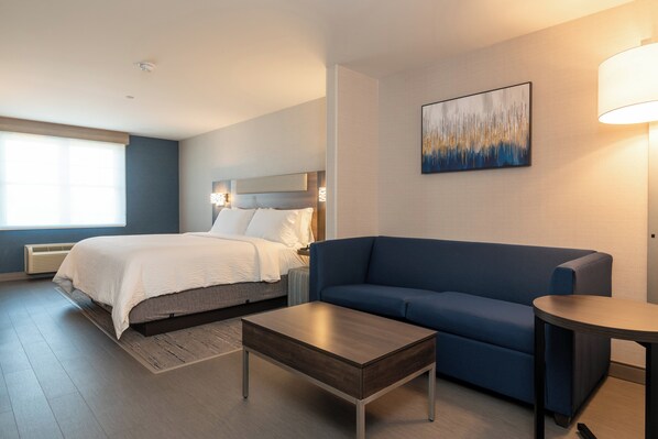 Ein modernes Hotelzimmer mit einem Bett, einem blauen Sofa, einem Holztisch und einem Bild an der Wand.